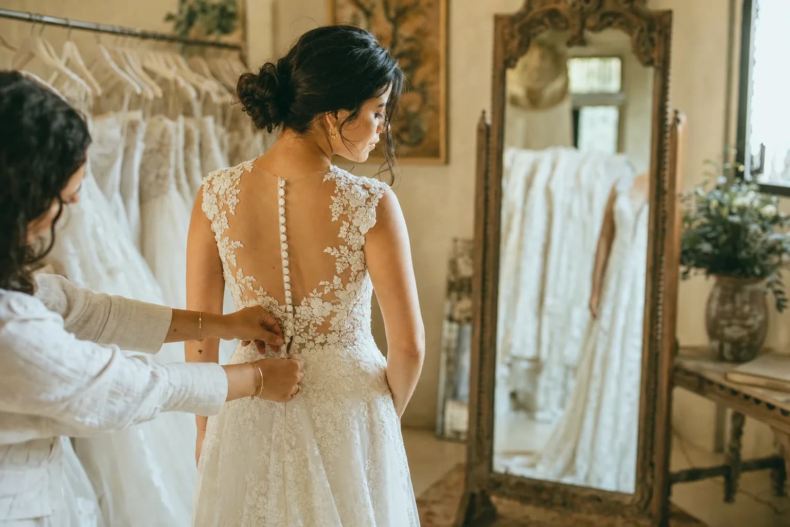 Novia mexicana probándose un vestido de novia marfil de encaje frente al espejo en un atelier