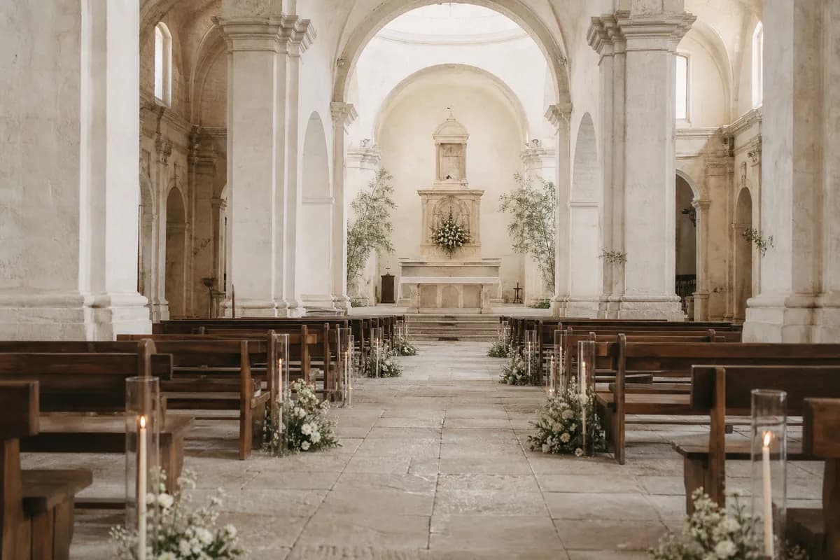 Pasillo de iglesia minimalista con pocos arreglos blancos, velas altas y arquitectura de piedra