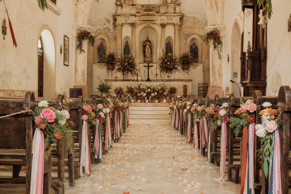 Pasillo de iglesia boho con petalos en el piso y cintas de colores en las bancas
