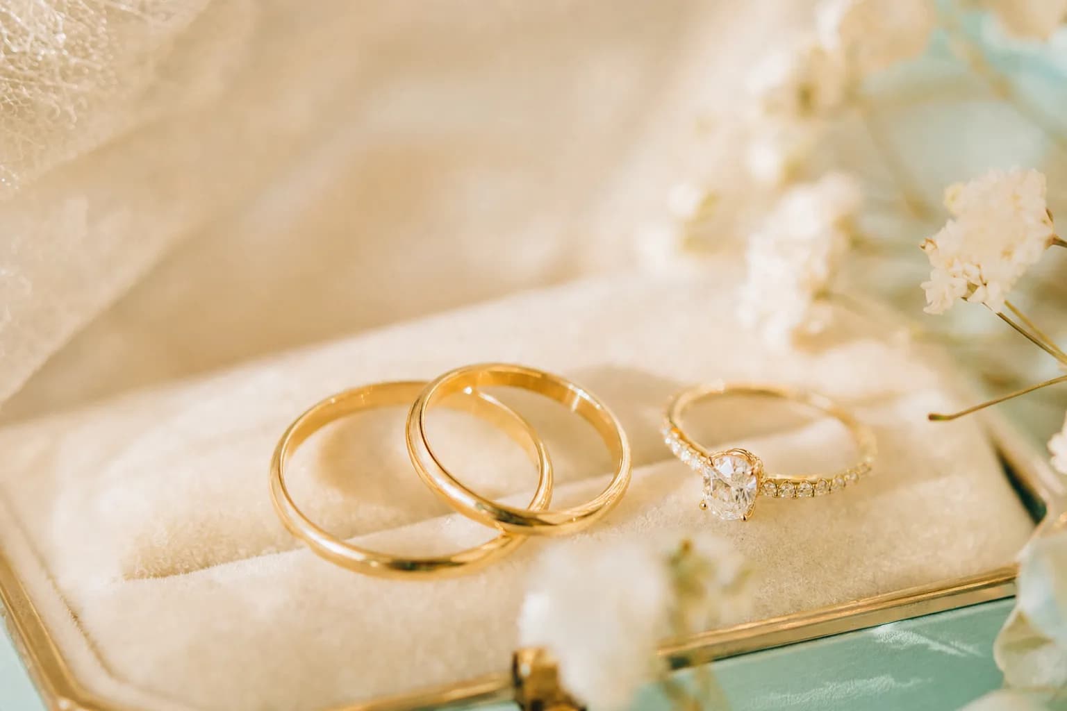 Anillos de boda de oro y anillo de compromiso con piedra sobre terciopelo crema con luz natural