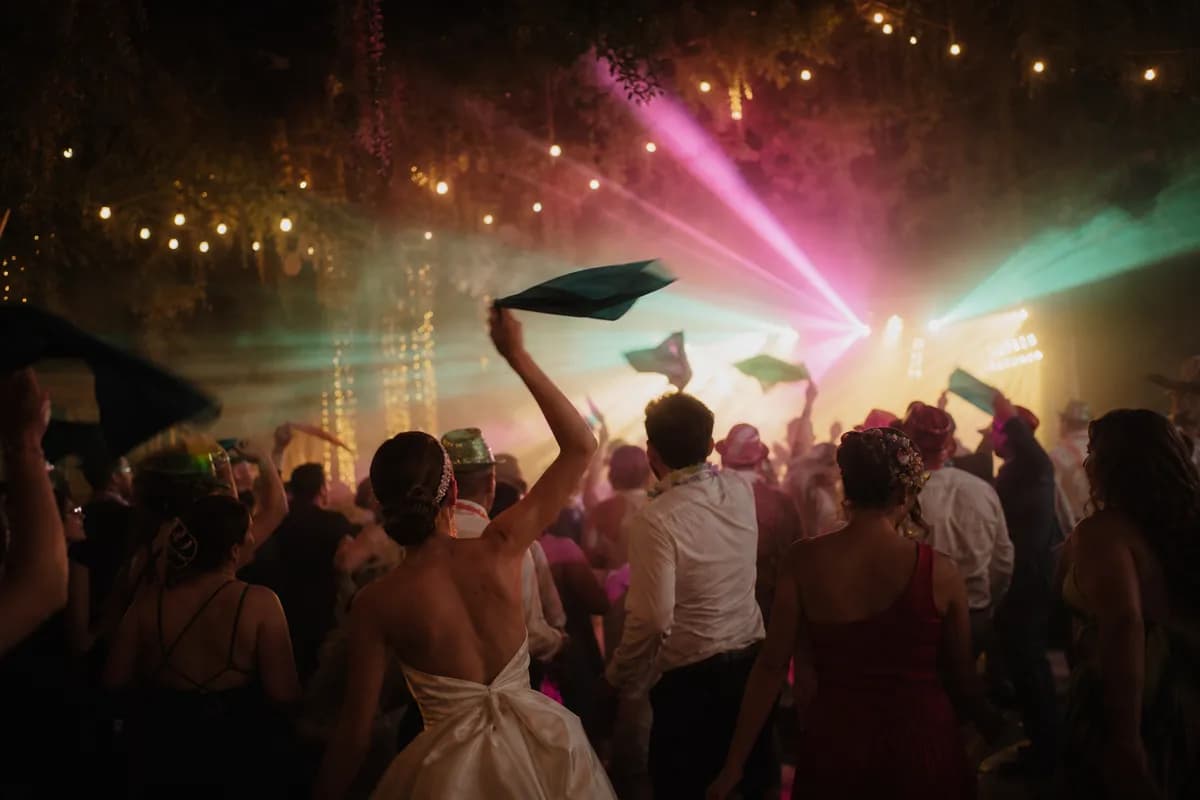 Invitados bailando en la hora loca de una boda bajo luces LED de colores y humo de máquina