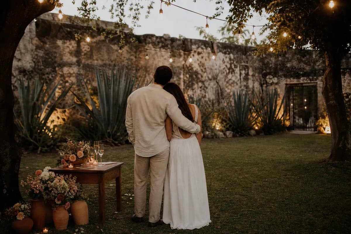 Pareja abrazada tras la pedida en jardín de hacienda mexicana con guirnaldas de luces